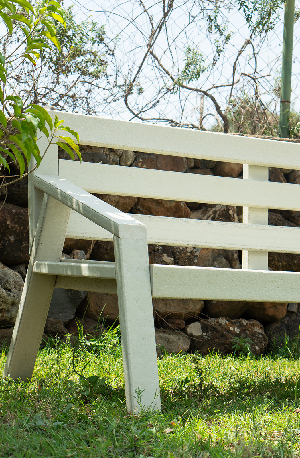 Close-up of a cream recycled plastic garden bench on a lawn beside a stone wall