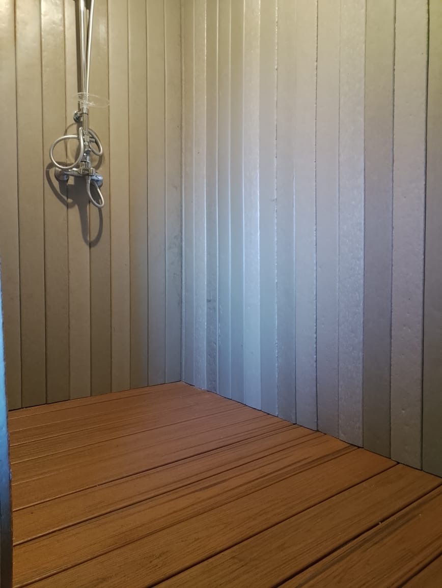 Corner of a camp shower clad in recycled plastic boards with timber-tone recycled decking floor