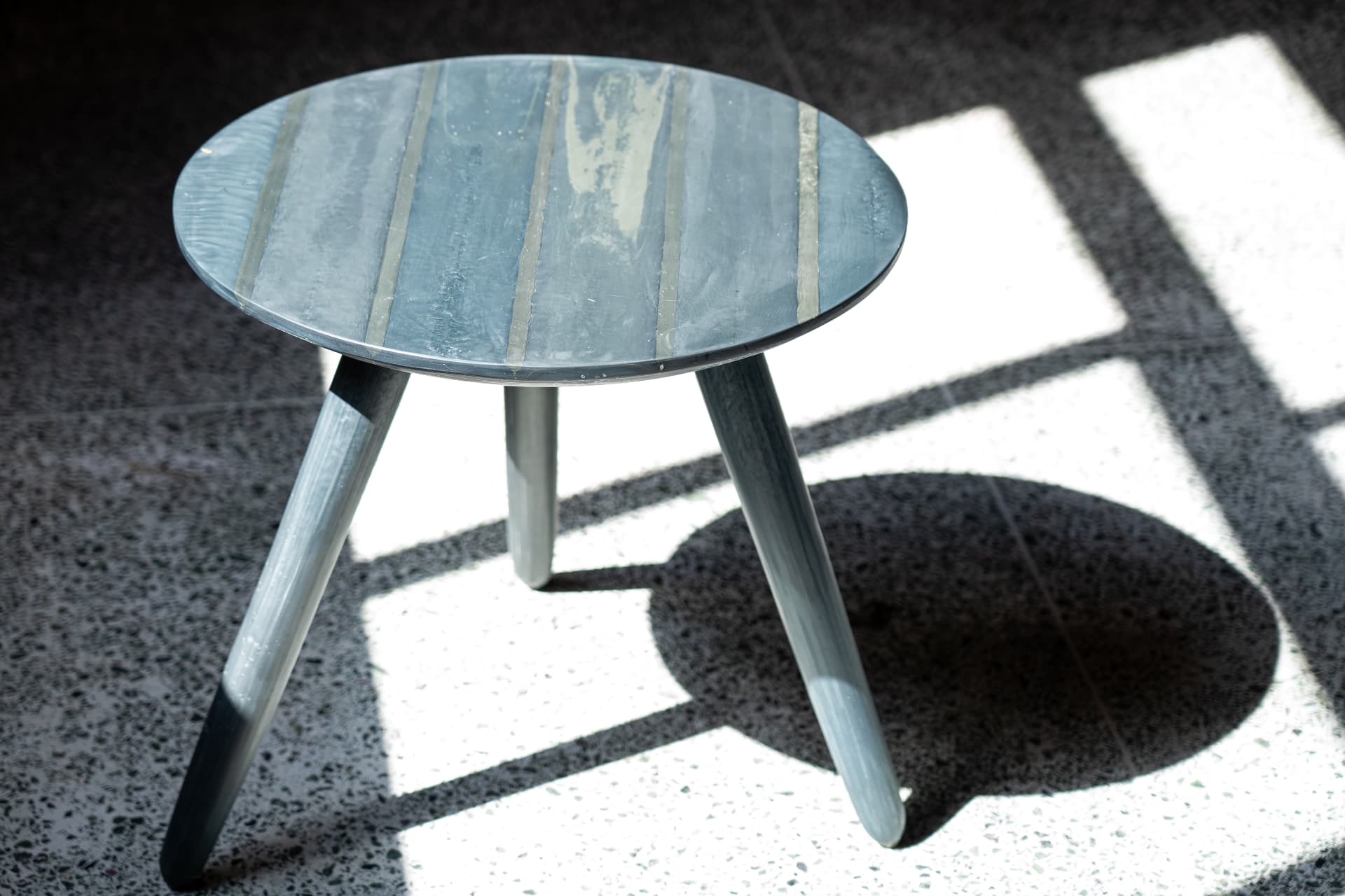 Round recycled plastic side table with a marbled grey top and tapered legs in raking daylight